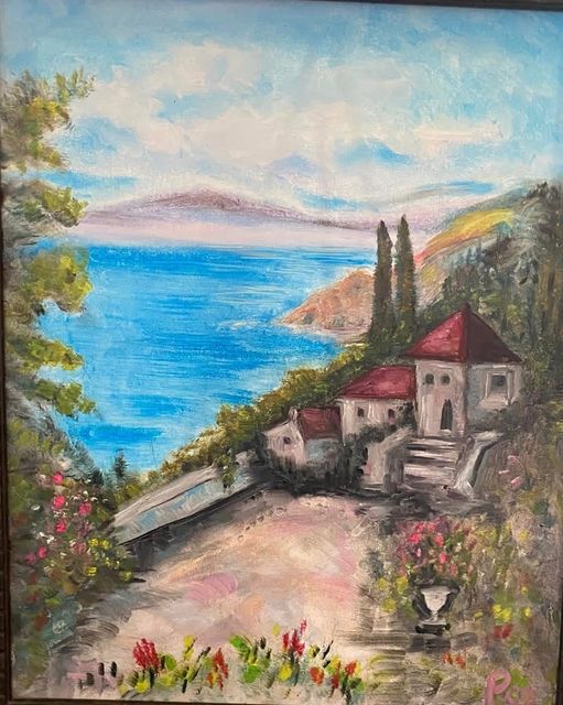 A hillside village with red roofs and cypress trees above a blue bay